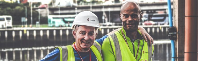 selective focus photography of two men standing side by side wearing green reflective vests